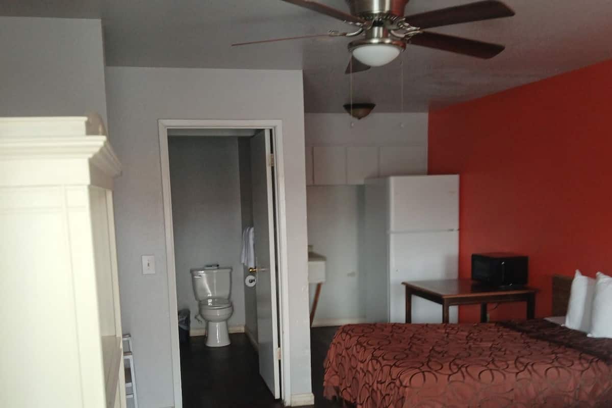 A hotel room with a bed, a desk, a chair, a television, a wardrobe, and a ceiling fan.