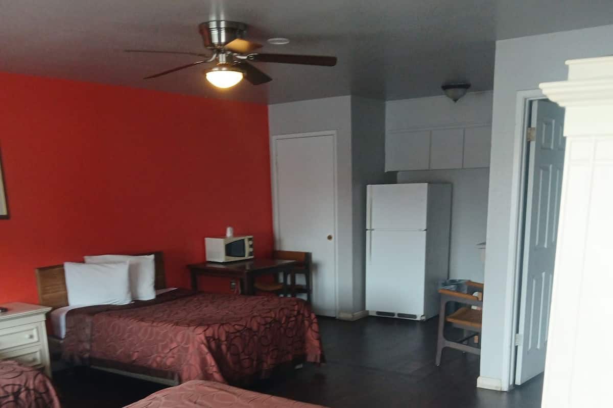 A room with two beds, a ceiling fan, a microwave, a refrigerator, and a small table with chairs.