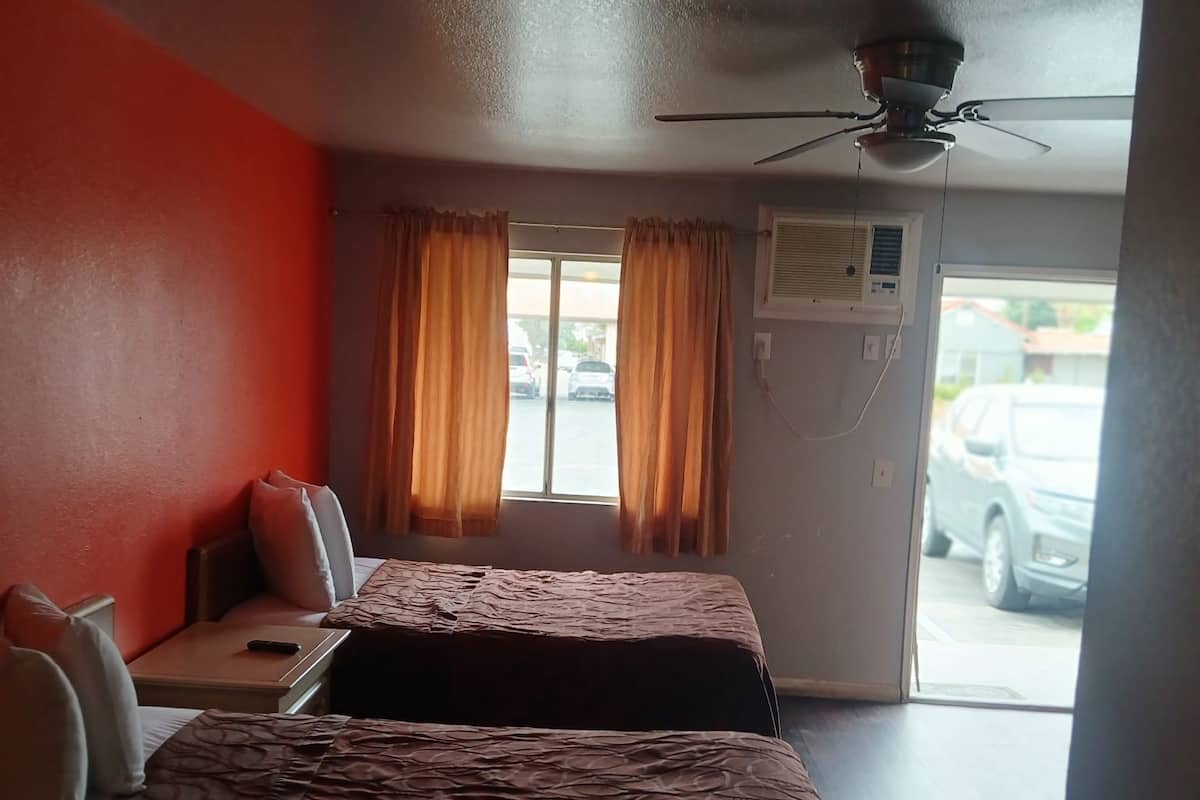 A hotel room with two beds, a desk, a chair, a ceiling fan, and a window with curtains.