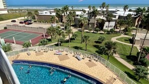 A pool area with a tennis court, palm trees, and a view of the ocean. - 3rd Coast Getaways - Sunchase IV 330 (South Padre Island)