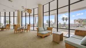 A spacious indoor area with large windows, wicker furniture, and a ceiling fan. - 3rd Coast Getaways - Sunchase IV 330 (South Padre Island)