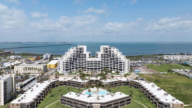 A large hotel with a central courtyard and a pool, surrounded by a coastal view and a bridge in the background. - 3rd Coast Getaways - Sunchase IV 330 (South Padre Island)