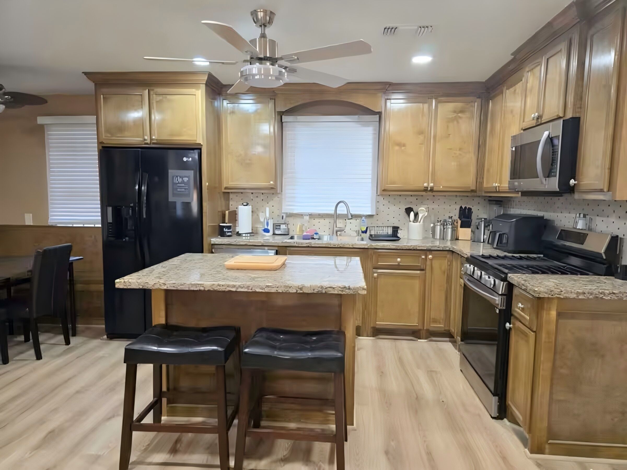A kitchen with wooden cabinets, a black refrigerator, a microwave, a stove, and a ceiling fan.