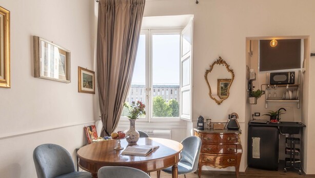 Un comedor con una mesa redonda, sillas, un florero y una ventana con cortinas.