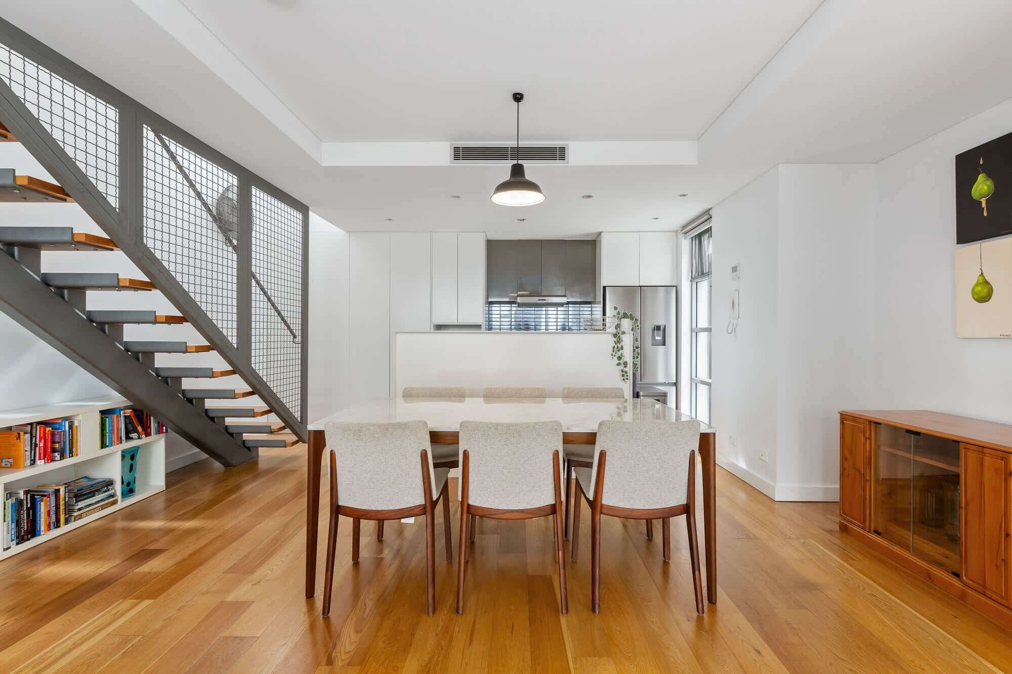 A modern kitchen with white cabinets, a central island, and a dining area with wooden chairs.