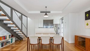 A modern kitchen with white cabinets, a central island, and a dining area with wooden chairs. - Spacious 2-Bed Retreat in Rosebery (Rosebery)