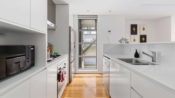 A modern kitchen with white cabinetry, a stainless steel sink, and a microwave. - Spacious 2-Bed Retreat in Rosebery (Rosebery)