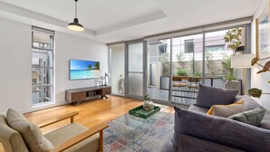A modern living room with a flat-screen TV, a glass coffee table, and a grey sofa. - Spacious 2-Bed Retreat in Rosebery (Rosebery)