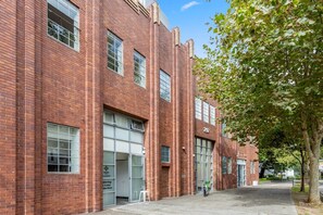 A red brick building with large windows and a tree-lined street. - Spacious 2-Bed Retreat in Rosebery (Rosebery)