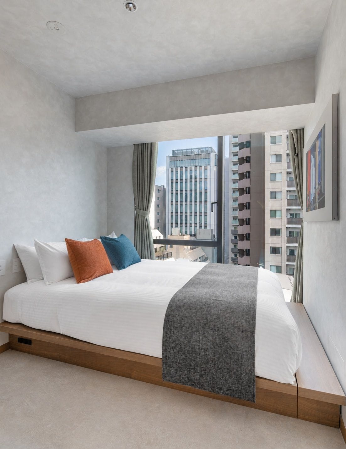Ein modernes Hotelzimmer mit einem großen Bett, Blick auf hohe Gebäude und einem mit Vorhängen versehenen Fenster.