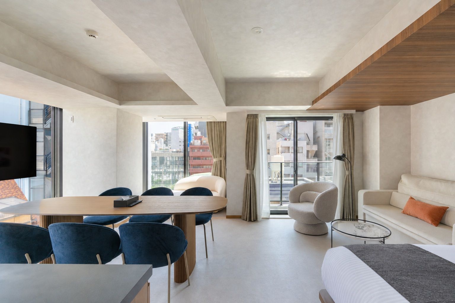 Ein modernes Hotelzimmer mit Essbereich, einer Couch, einem Bett und Blick auf die Stadtlandschaft.