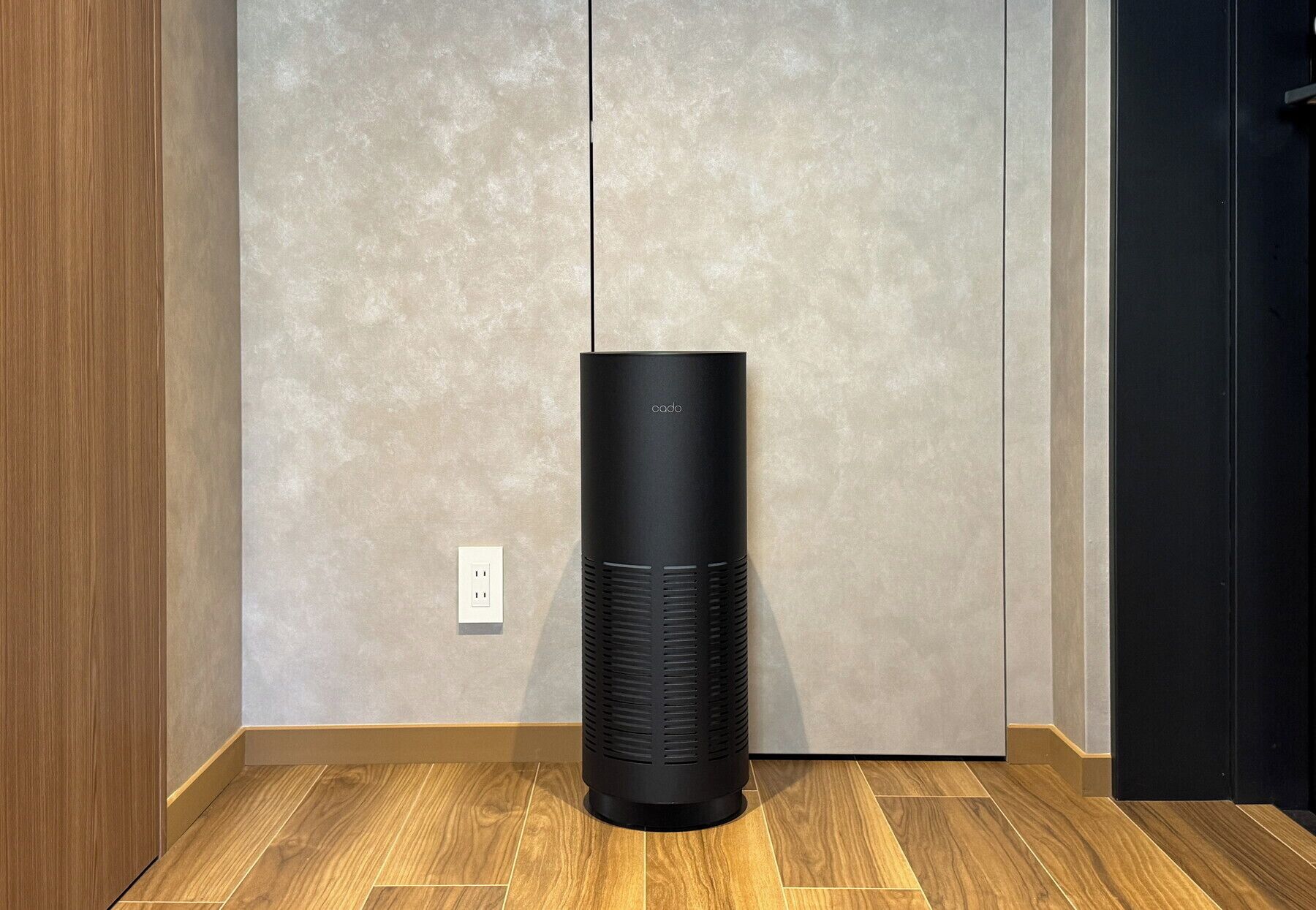 A black cylindrical device on a wooden floor with a textured wall and a door in the background.