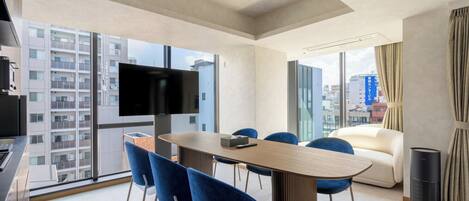 A modern hotel room with a dining area, a sofa, a TV, and a city view.
