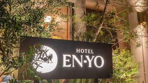 Schild für Hotel EN-YO mit Logo, umgeben von Grünpflanzen und Felsen.