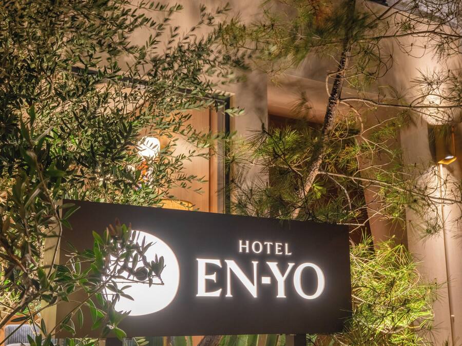 Schild für Hotel EN-YO mit Logo, umgeben von Grünpflanzen und Felsen.