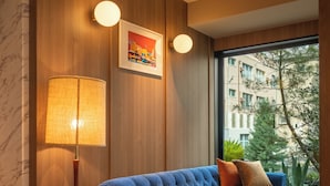 Ein modernes Wohnzimmer mit einem blauen Sofa, einem runden Holztisch, einer Stehlampe und einem großen Fenster mit Blick auf Gebäude und Bäume.