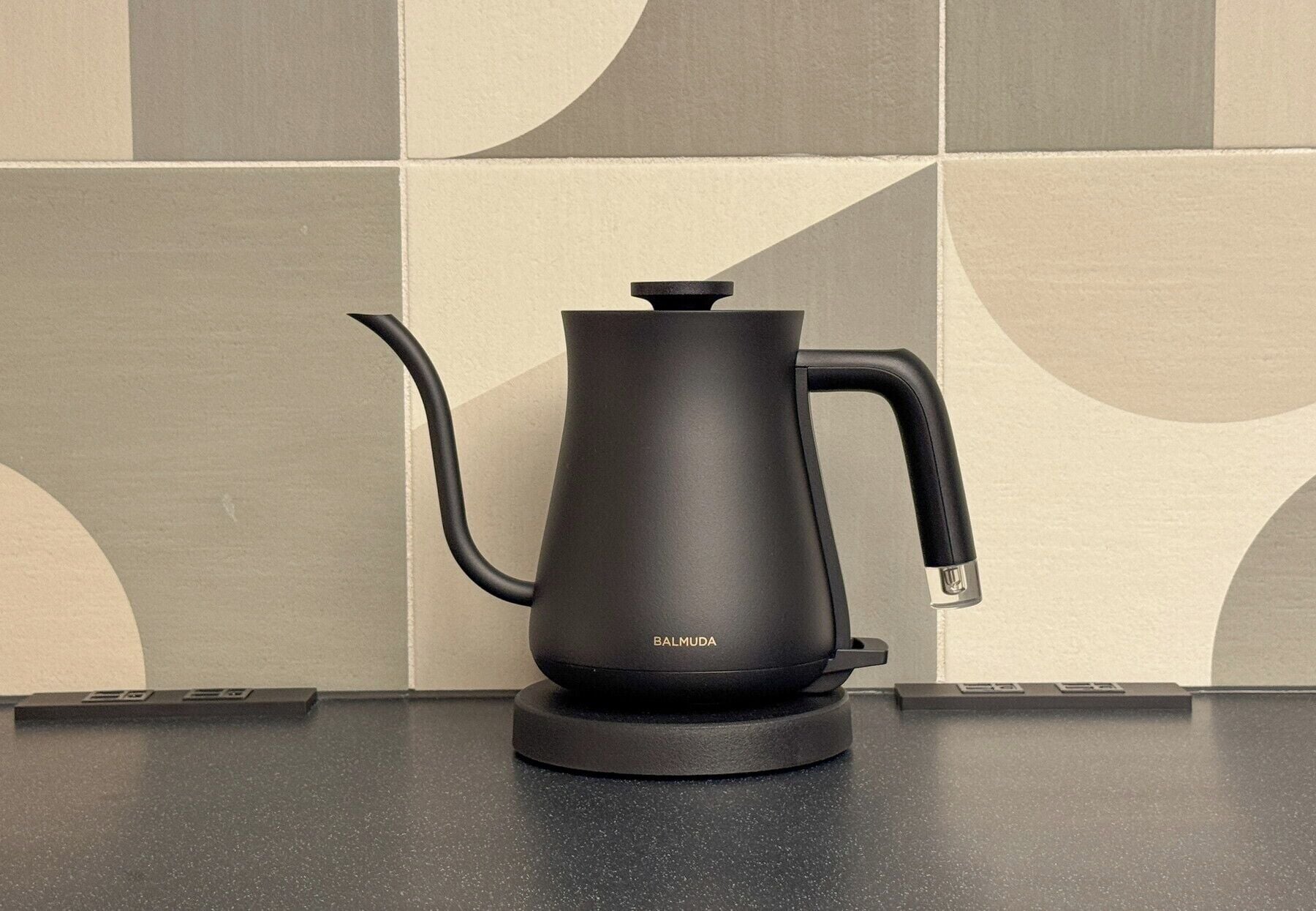 Eine schwarze elektrische Wasserwafle mit Ausguss und Griff auf einer schwarzen Arbeitsplatte.