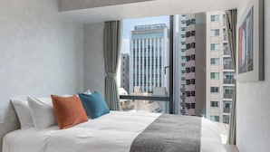 Ein modernes Hotelzimmer mit einem großen Bett, Blick auf hohe Gebäude und einem mit Vorhängen versehenen Fenster.