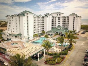 Ein mehrstöckiges Hotel mit Poolbereich, Palmen und Blick auf den Ozean.