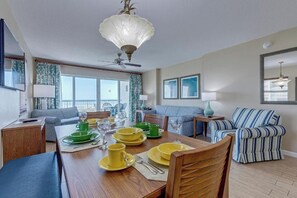 Ein Essbereich mit einem Holztisch, gedeckt für vier Personen, einem Deckenventilator und einem großen Fenster mit Vorhängen.