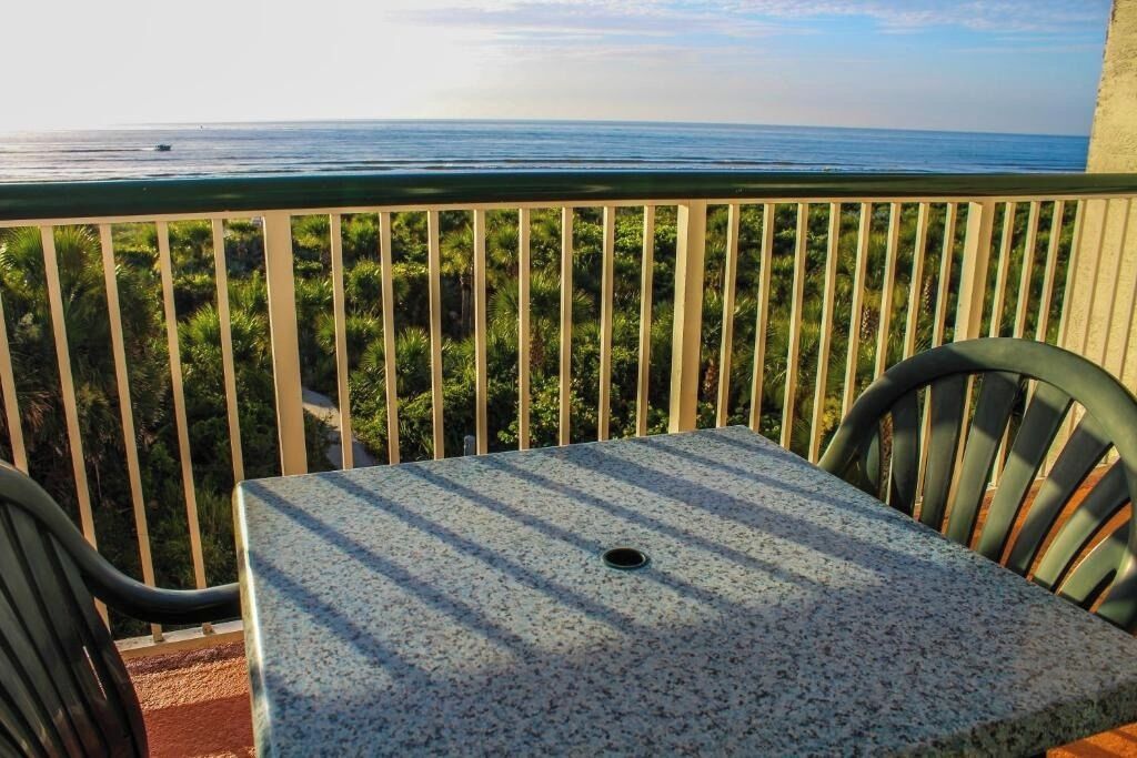 En balkon med et bord og stole, ud til udsigt over havet og grøn vegetation.