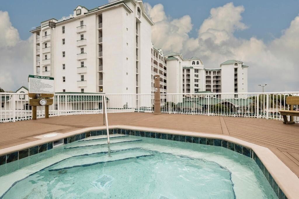 A pool area with a sign indicating spa rules, surrounded by a wooden deck and white railings.