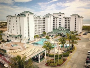 Ein mehrstöckiges Hotel mit Poolbereich, Palmen und Blick auf den Ozean.