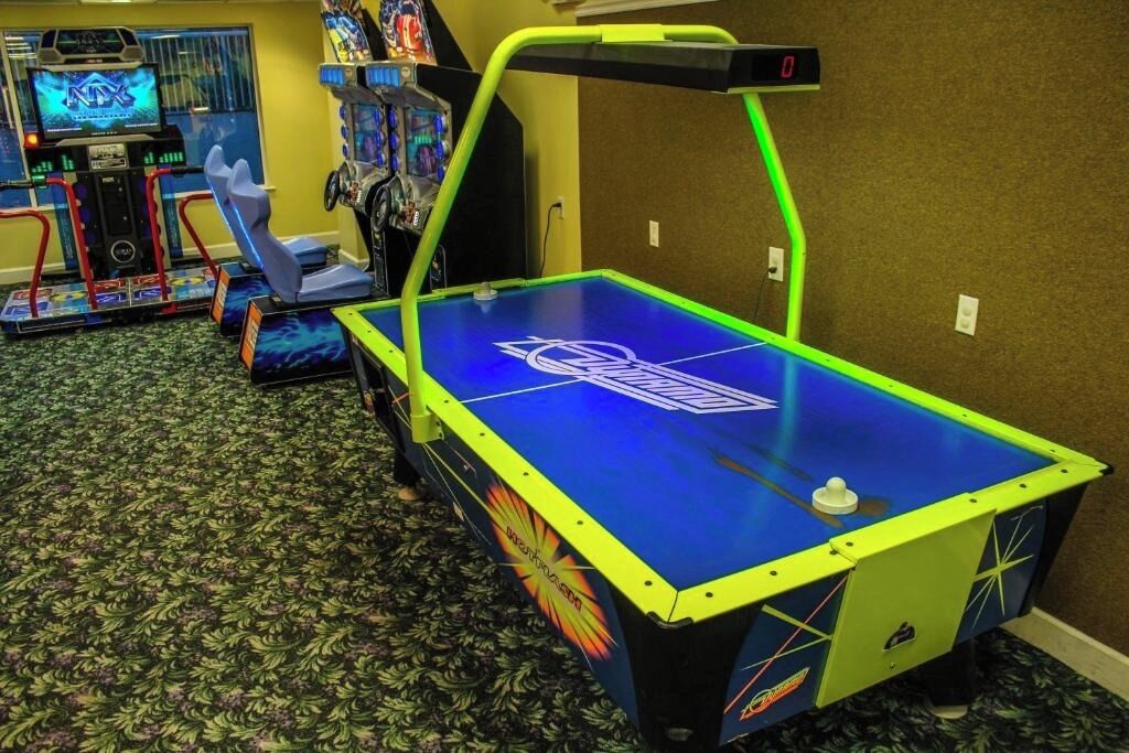 Ein Billardtisch mit neonfarbenem Rahmen und einer digitalen Anzeigetafel in einem Raum voller Arcade-Spiele.