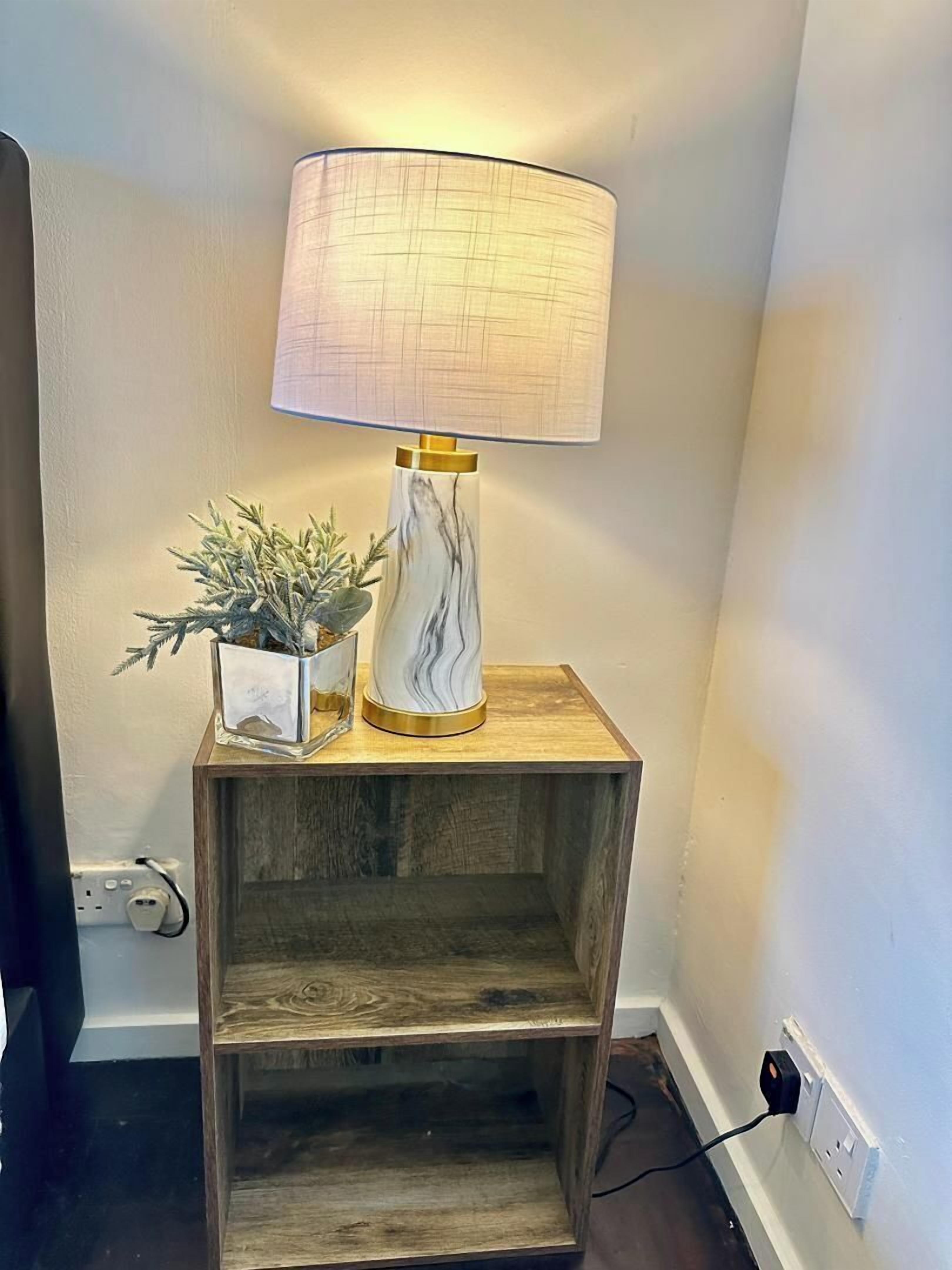 Une table de chevet avec une lampe, une petite plante et un vase décoratif.