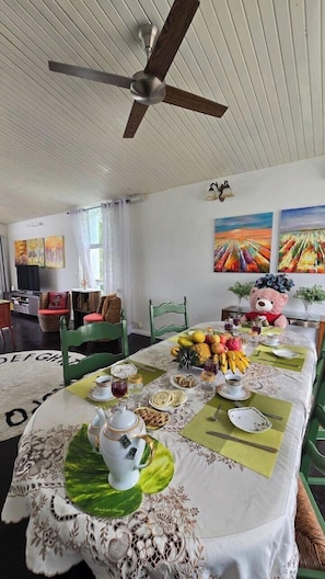 Un coin repas avec une table mise pour le repas, des chaises, un ventilateur de plafond et des œuvres d’art accrochées aux murs.