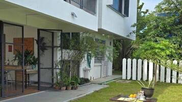 A modern building with a balcony, outdoor seating area with tables and benches, and a garden with potted plants.