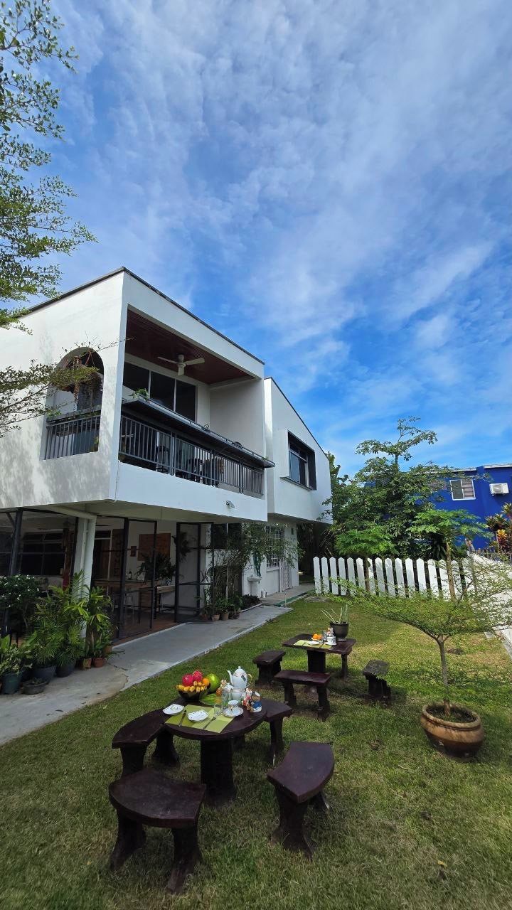 A modern two-story building with a balcony, outdoor seating area with tables and benches, and a white picket fence in the background.