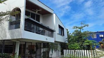 A modern two-story building with a balcony, outdoor seating area with tables and benches, and a white picket fence in the background.
