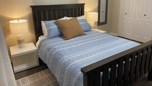 A bedroom with a bed, two bedside tables with lamps, a wall-mounted mirror, and a wardrobe. - Spacious 2 BR Suite, Family Friendly, near Colwood Waterfront, Royal Roads Univ (Victoria)