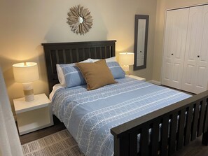Een slaapkamer met een bed, twee nachtkastjes met lampen, een spiegel aan de muur en een kledingkast.