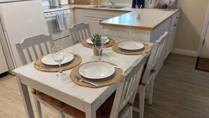 A dining table set with plates, cutlery, and glassware, surrounded by white chairs in a kitchen with white cabinets and a wooden countertop. - Spacious 2 BR Suite, Family Friendly, near Colwood Waterfront, Royal Roads Univ (Victoria)