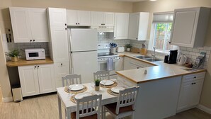 A kitchen with white cabinets, a microwave, a refrigerator, a dining table with chairs, and a window. - Spacious 2 BR Suite, Family Friendly, near Colwood Waterfront, Royal Roads Univ (Victoria)