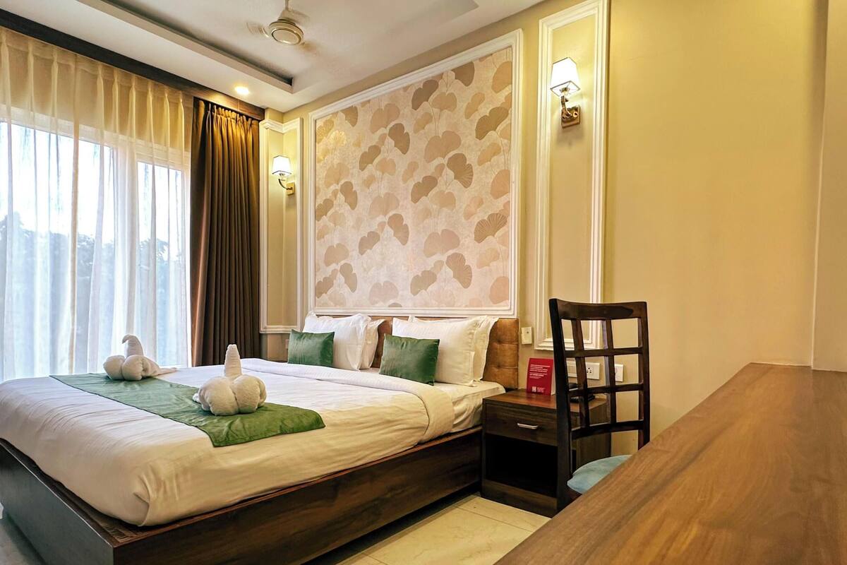 A hotel room with a bed, bedside table, chair, and a view of the outdoors.