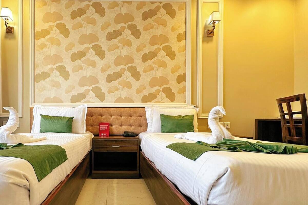 A hotel room with two beds, a nightstand, a red fire extinguisher, and a wooden chair.