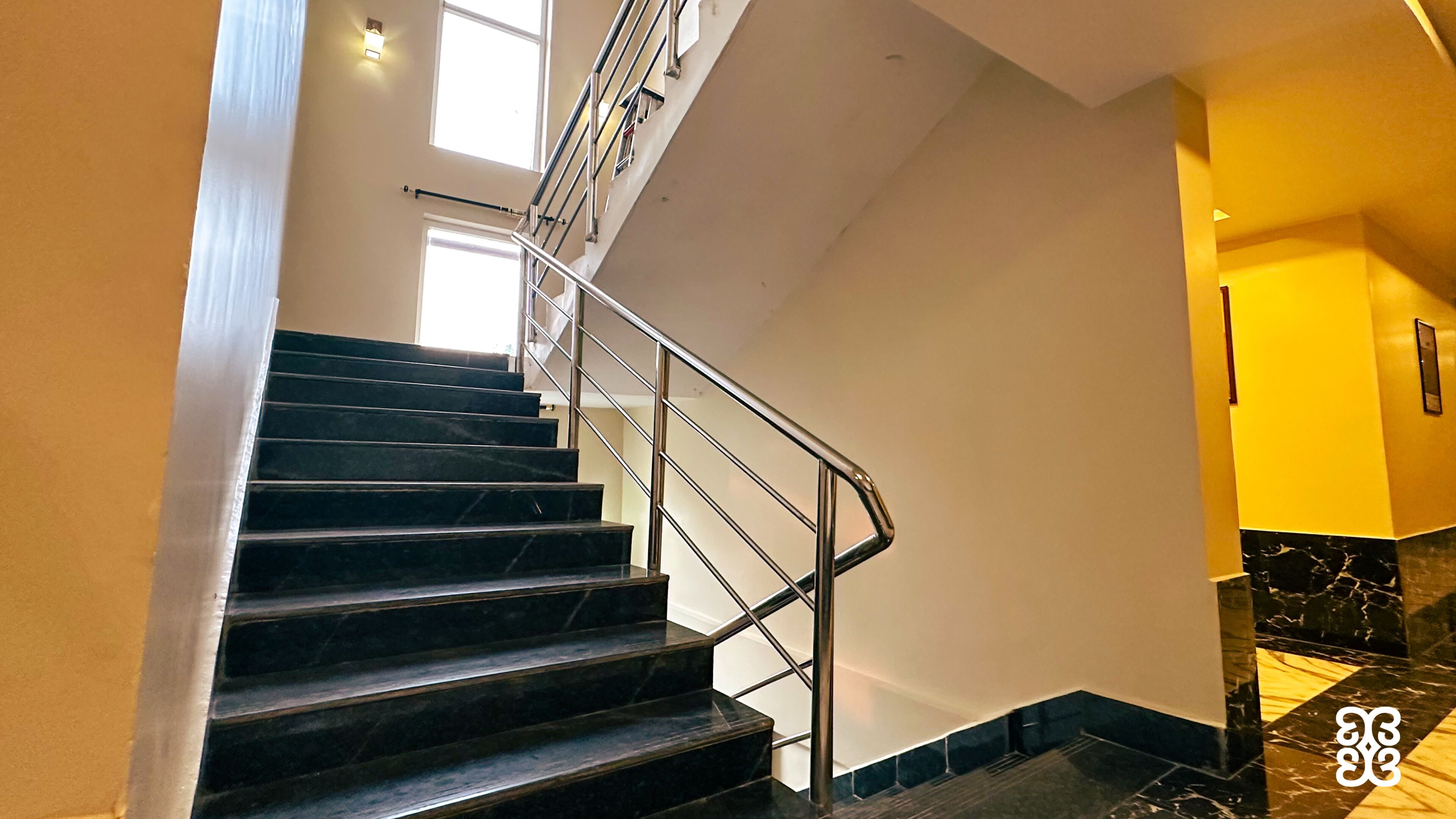 A staircase with a metal railing, a marble floor, and a light fixture on the wall.