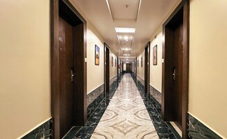 Un pasillo largo y estrecho con suelo de mármol, puertas de madera y cuadros en las paredes.