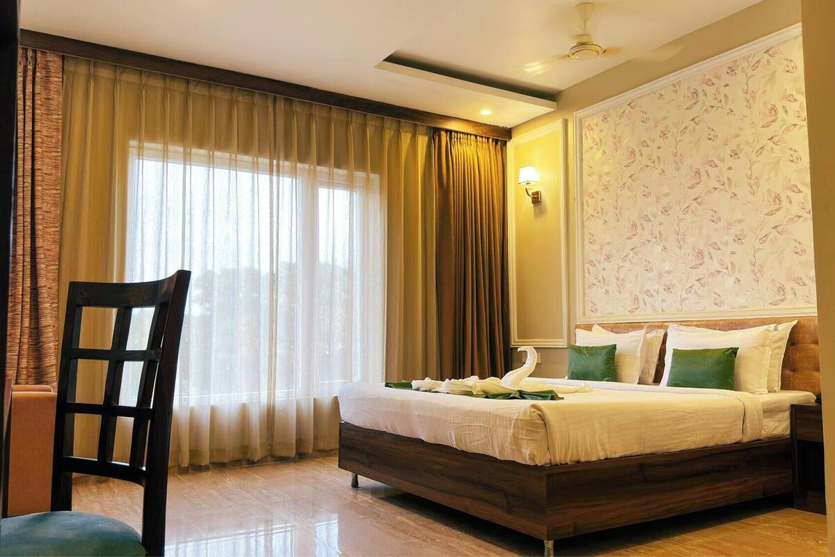A bedroom with a bed, a chair, a window with curtains, a wall-mounted light, and a floral wallpaper.