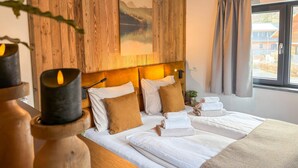 Quarto de hotel com painéis de madeira, cama com roupa de cama branca, pintura na parede e janela com cortinas.