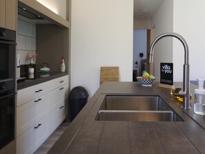 A modern kitchen with a stainless steel sink, white cabinetry, and a bowl of fruit on the counter.