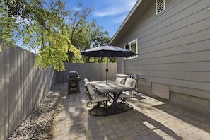 Eine Terrasse mit Tisch, Stühlen, Sonnenschirm und Grill.