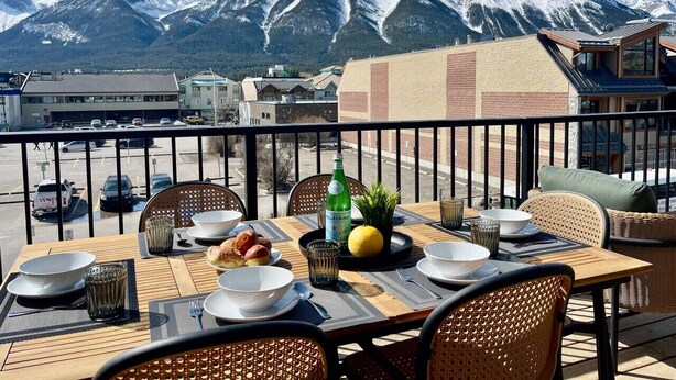 A dining table set outdoors with a mountain view, chairs, and a bottle of water. - RETRORIDGE - DOWNTOWN - ROOFTOP HOT TUB (Canmore)