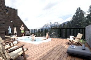 A wooden deck with a hot tub, lounge chairs, and a view of mountains. - RETRORIDGE - DOWNTOWN - ROOFTOP HOT TUB (Canmore)
