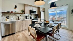 A modern kitchen with a dining area, large windows, and a view. - RETRORIDGE - DOWNTOWN - ROOFTOP HOT TUB (Canmore)
