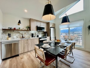 A modern kitchen with a dining area, large windows, and a view. - RETRORIDGE - DOWNTOWN - ROOFTOP HOT TUB (Canmore)