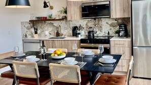 A modern kitchen with a marble backsplash, wooden cabinets, a stainless steel refrigerator, and a dining area with a black table and wicker chairs. - RETRORIDGE - DOWNTOWN - ROOFTOP HOT TUB (Canmore)